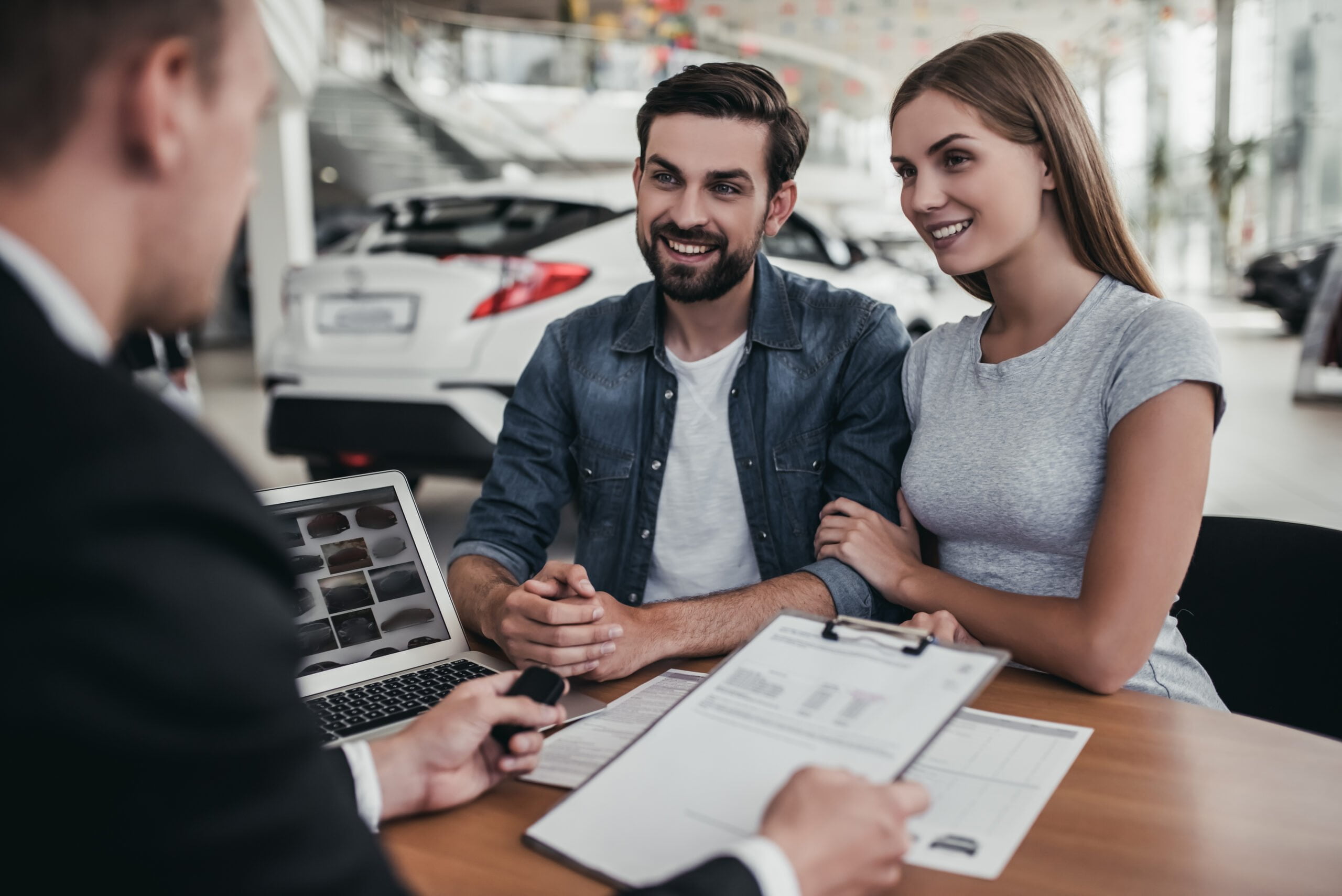 Happy beautiful couple is buying a new car at dealership.